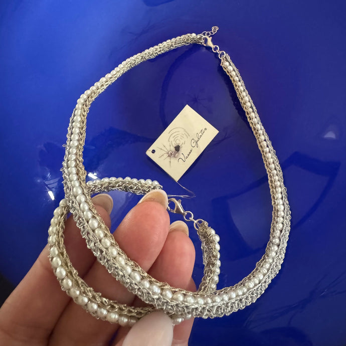 Silver and pearl bracelet held by a hand with a blue background