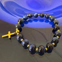 Black beaded bracelet with a yellow cross charm on a reflective surface