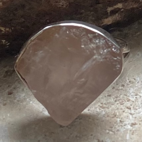 A triangular shaped rose quartz ring on a textured surface.