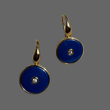 Pair of gold earrings with blue circular stones on a gray background