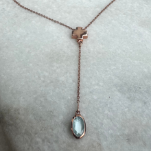 Necklace with a cross pendant and teardrop-shaped gemstone on a marble surface