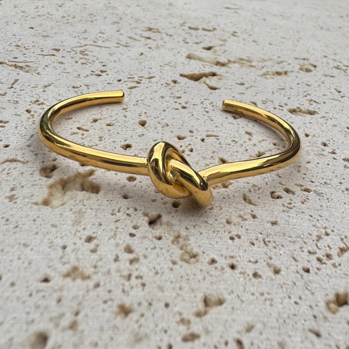 Gold knot bangle on a textured beige surface