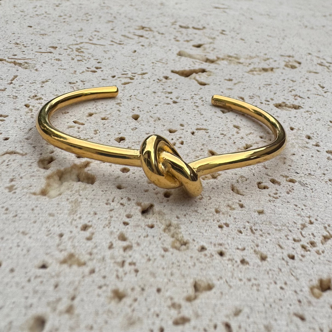 Gold knot bangle on a textured beige surface