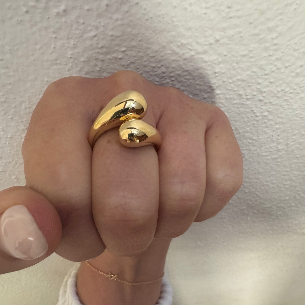 Gold heart-shaped ring on a finger against a neutral background