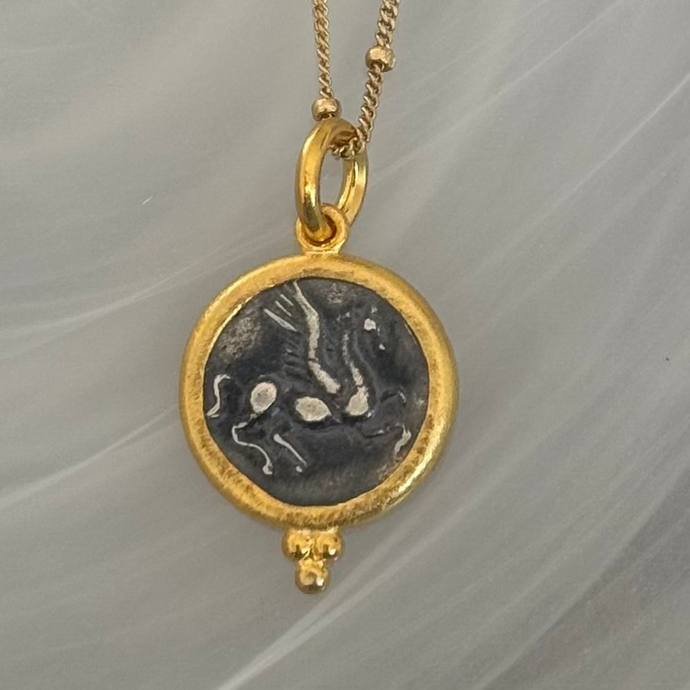 Gold necklace with a round pendant featuring an engraved design on a gray background