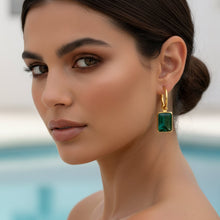 Woman wearing a gold earring with a green gemstone by a pool