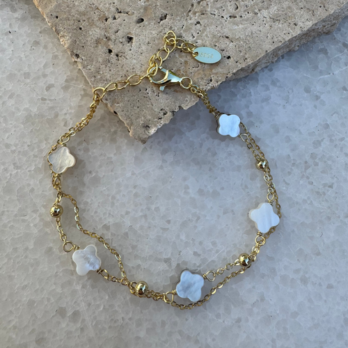 Gold bracelet with white floral charms on a stone surface