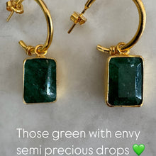Gold earrings with green semi-precious stones on a marble surface