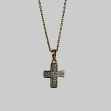 Gold necklace with a cross pendant on a light gray background
