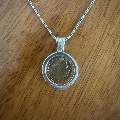 Silver pendant with a coin design on a wooden surface