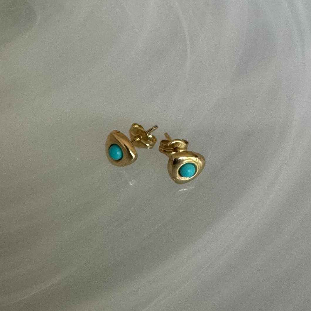 Gold earrings with turquoise stones on a gray marble background