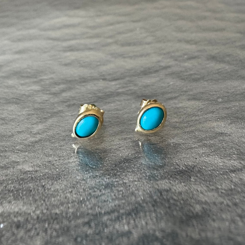 Gold earrings with turquoise stones on a gray surface