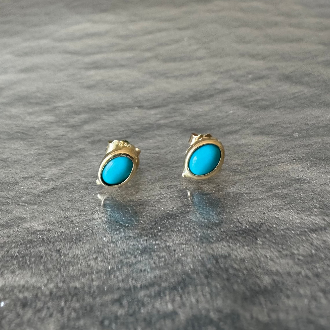 Gold earrings with turquoise stones on a gray surface