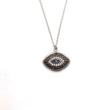 A turquoise mati-eye necklace with oxidised details, yellow and rose gold plating, and sterling silver, displayed against a beach backdrop.