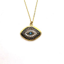 A turquoise mati-eye necklace with oxidised details, yellow and rose gold plating, and sterling silver, displayed against a beach backdrop.