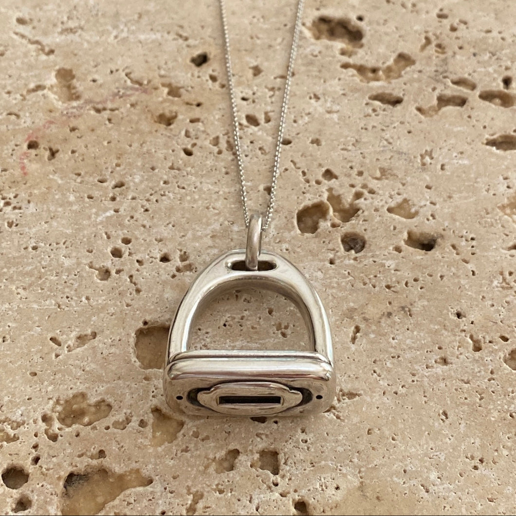 A large, bold sterling silver necklace with a stirrup-shaped pendant, displayed on a textured background.