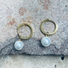 Pair of gold hoop earrings with pearl drops on a stone surface