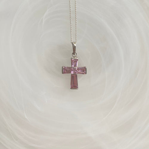 A pink crucifix necklace with sterling silver based cross and pink cubic zirconia stones, displayed against a light background.