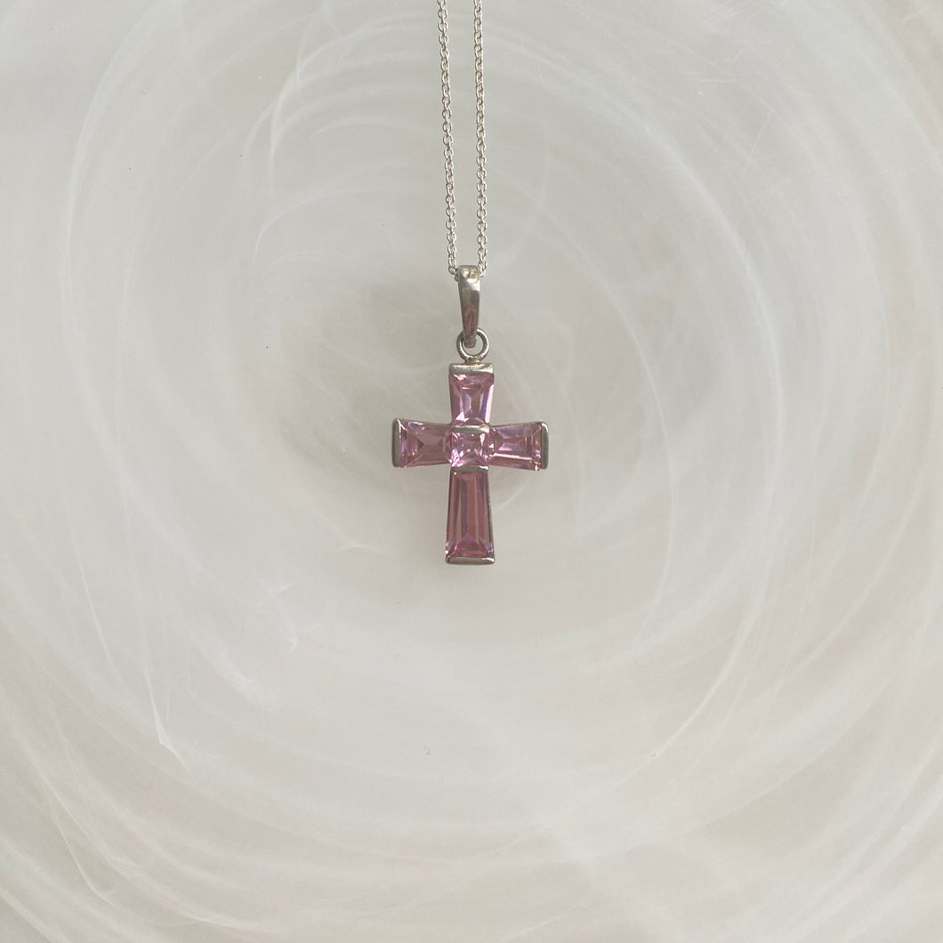 A pink crucifix necklace with sterling silver based cross and pink cubic zirconia stones, displayed against a light background.