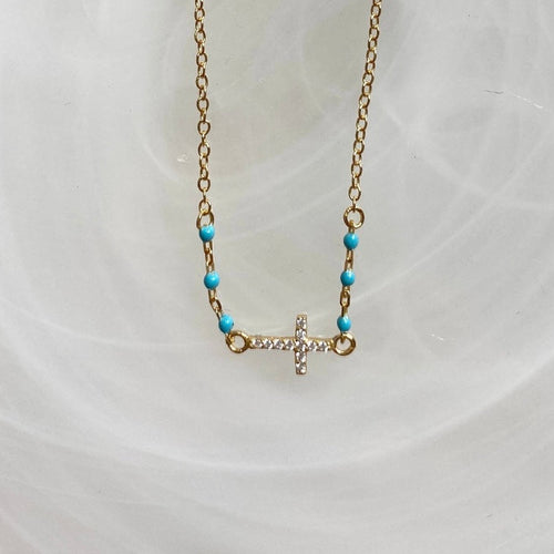 A gold-plated necklace with a petite cross pendant and turquoise beads on a white background.