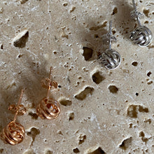 Two pairs of rose gold and silver earrings on a textured beige surface