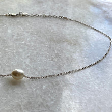 A sterling silver choker-necklace with a single white pearl on a marble surface.