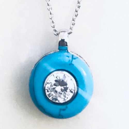 A round blue diamanté necklace with a central pendant and cubic zirconia inset, on a silver chain.
