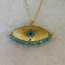 A gold vermeil necklace with turquoise beads and a blue centerpiece designed to resemble an eye, displayed on a mannequin.