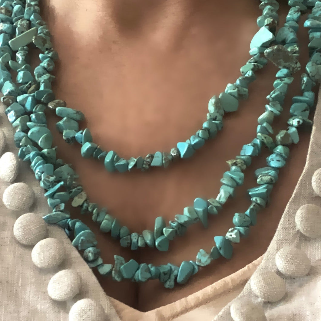 A three-layered turquoise bead necklace with a gold-plated clasp, displayed around a person's neck.
