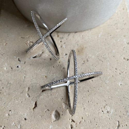 Two sterling silver rings with a cubic zirconia X shape design on a textured surface.