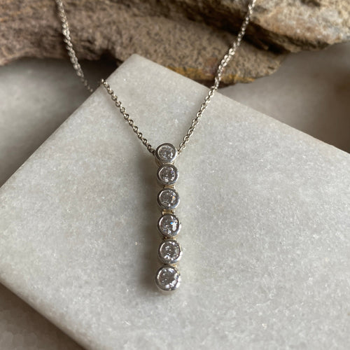 A sleek slim line diamanté necklace with round sparkly cubic zircons on a white surface, beside a rocky object.