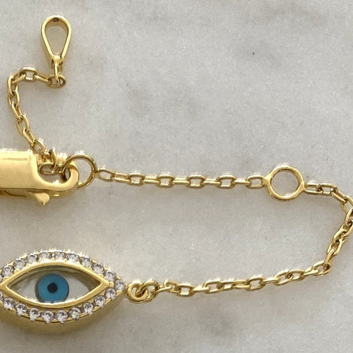 A bracelet featuring a mother of pearl with blue enamel eye centerpiece and a small cross along one side, set in 925 sterling silver.